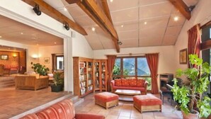 Ein geräumiger Wohnbereich mit Holzbalkendecke, einem roten Sofa, einem Couchtisch aus Holz und einem Bücherregal.