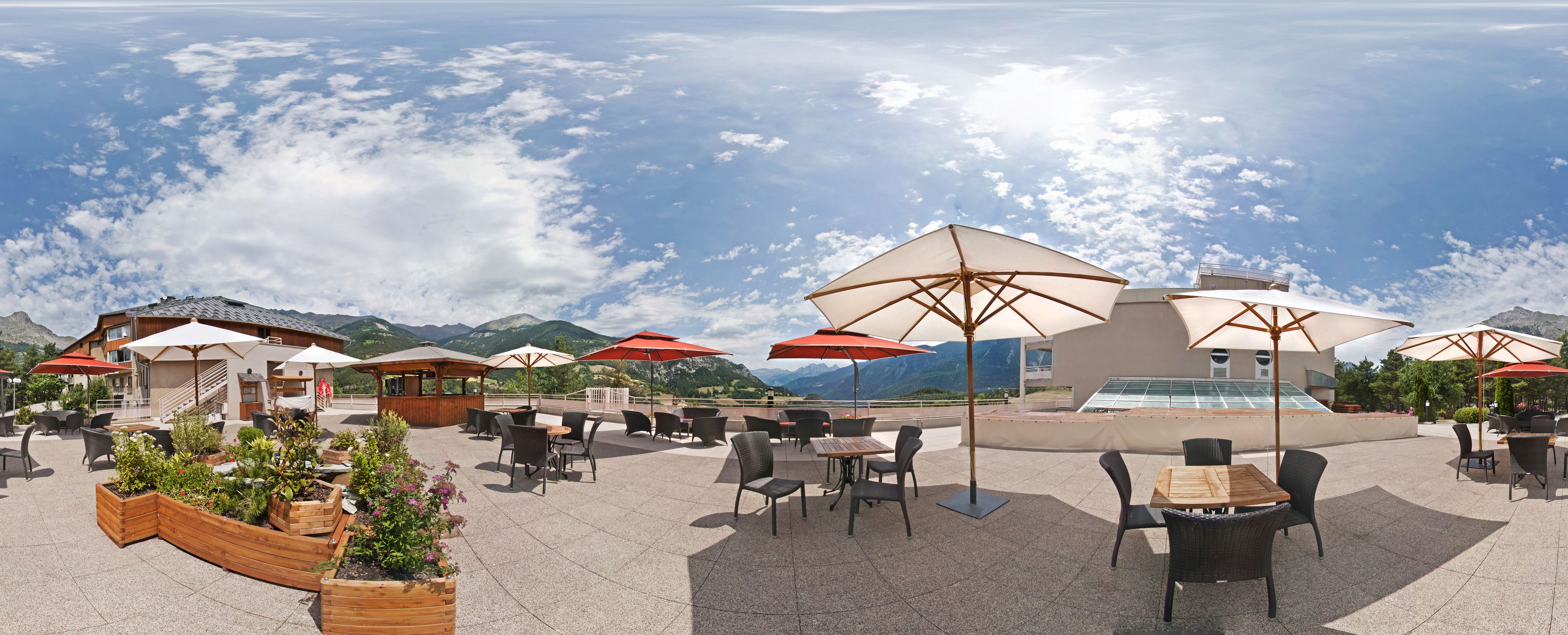 Une terrasse extérieure avec des tables et des chaises, des parasols et une vue sur les montagnes.