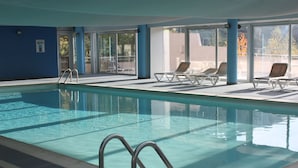 Ein hallenbad mit klarem Wasser, einer gefliesten Liegefläche und Liegestühlen.