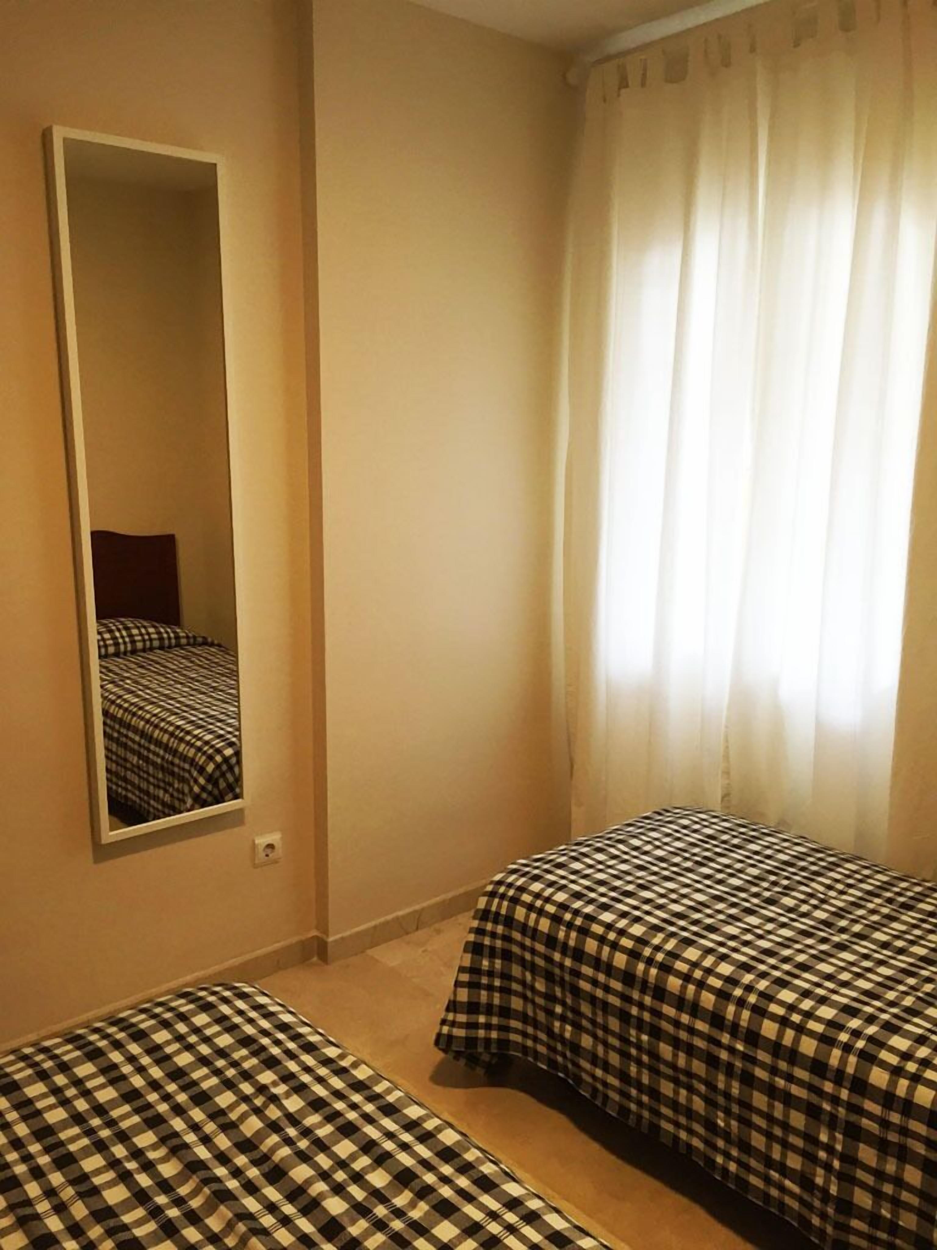 Une chambre avec deux lits, un miroir et une fenêtre avec des rideaux.
