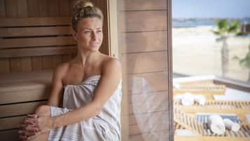 Une femme assise dans un sauna en bois, avec vue sur la plage.