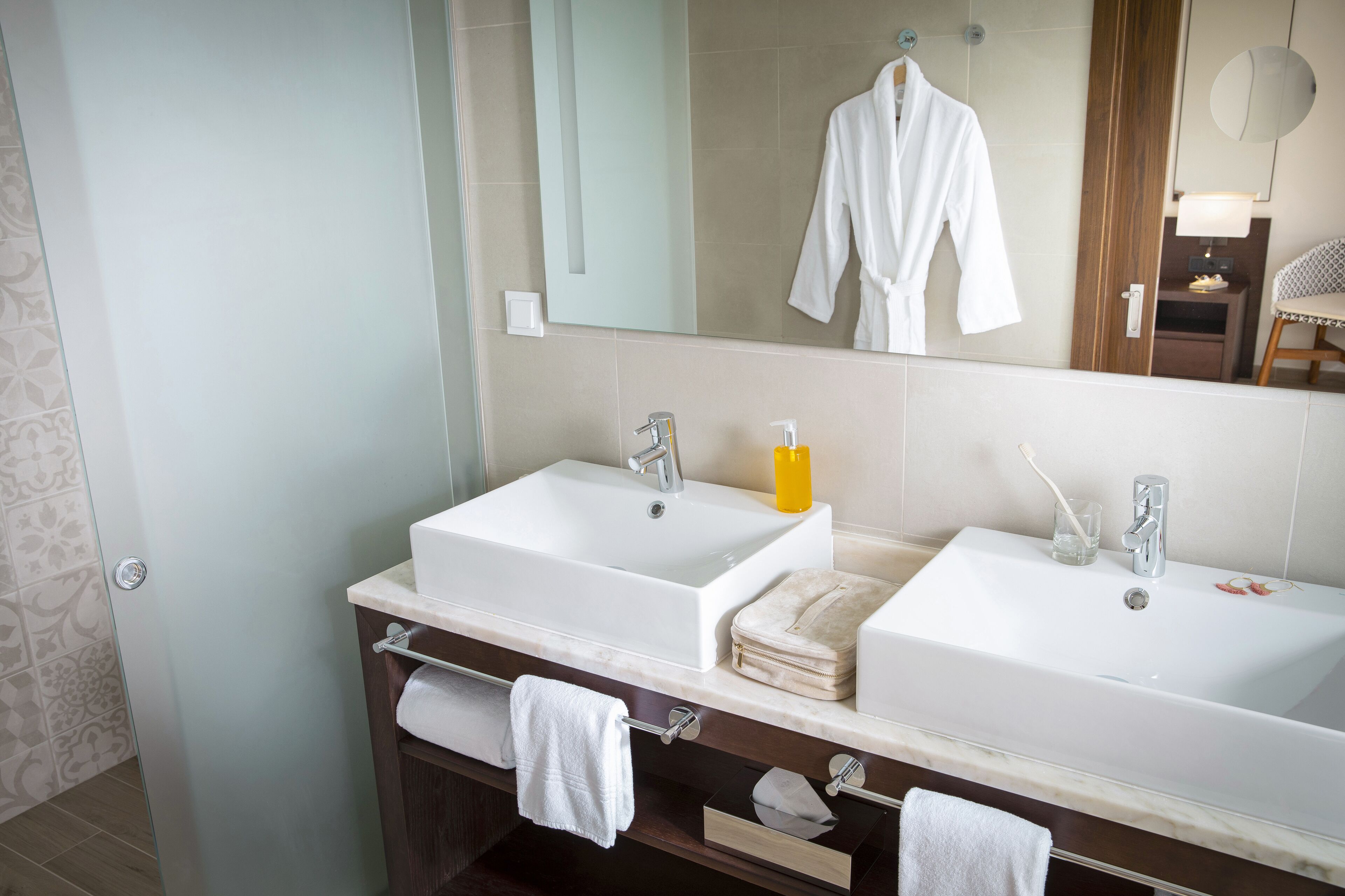 A bathroom with two sinks, a mirror, a robe, and a towel rack.