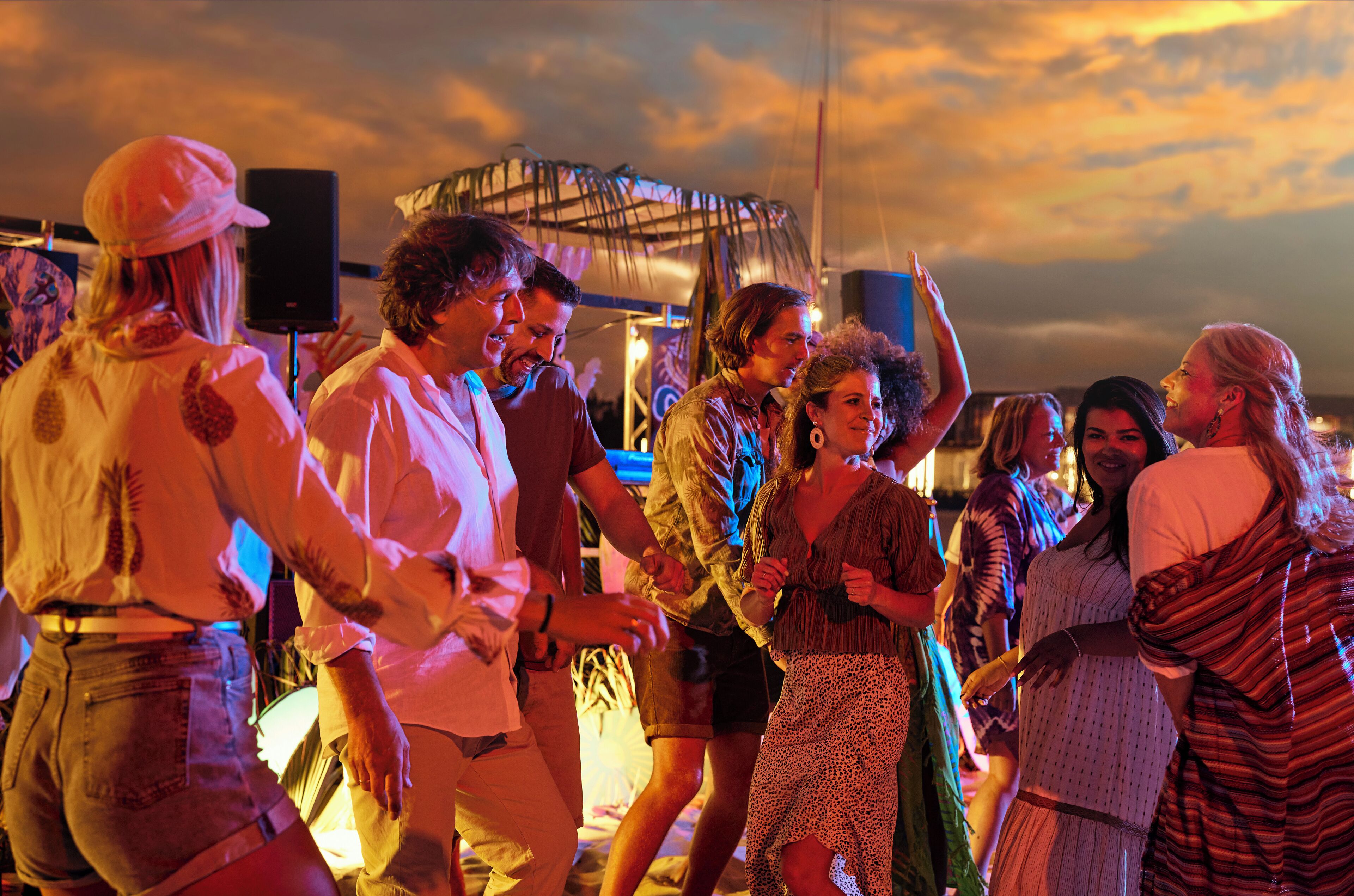 A group of people dancing at an outdoor event with a stage and speakers in the background.