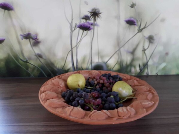 Une assiette en terre cuite ornée de poires, de raisins et d’un citron, posée sur une table en bois.