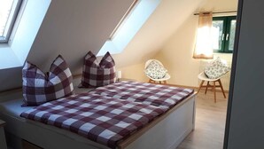 Ein gemütliches Schlafzimmer im Loft-Stil mit karierter Bettdecke, einem Oberlicht und Blick ins Freie.