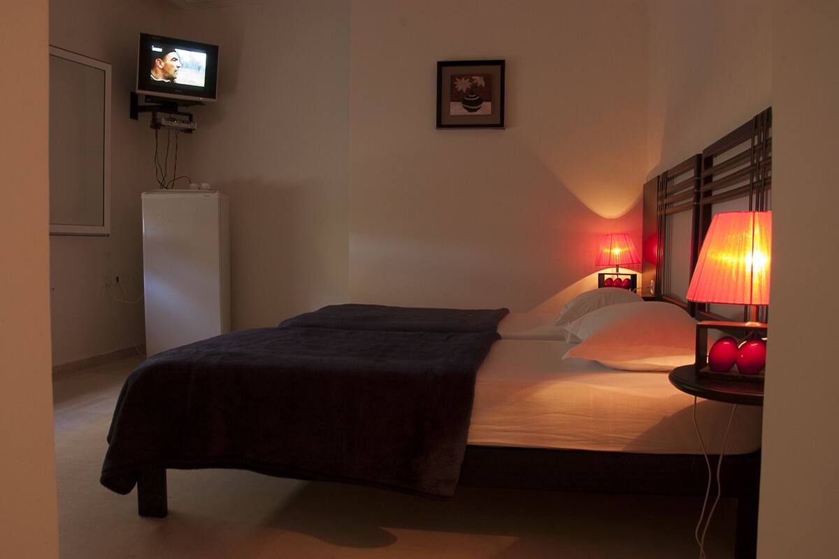 Ein Schlafzimmer mit einem Bett, Nachttischlampen, einem Fernseher auf einem Schrank und einem gerahmten Bild an der Wand.