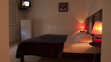 Un dormitorio con cama, lámparas de noche, televisor sobre un mueble y un cuadro en la pared.