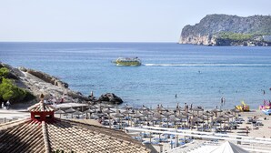 A beach with umbrellas, a boat, and rocky cliffs. - Hapimag Resort Paguera (Calvia)