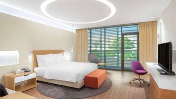 Ein modernes Hotelzimmer mit einem großen Bett, einem Schreibtisch, einem Sessel und einem Fernseher.