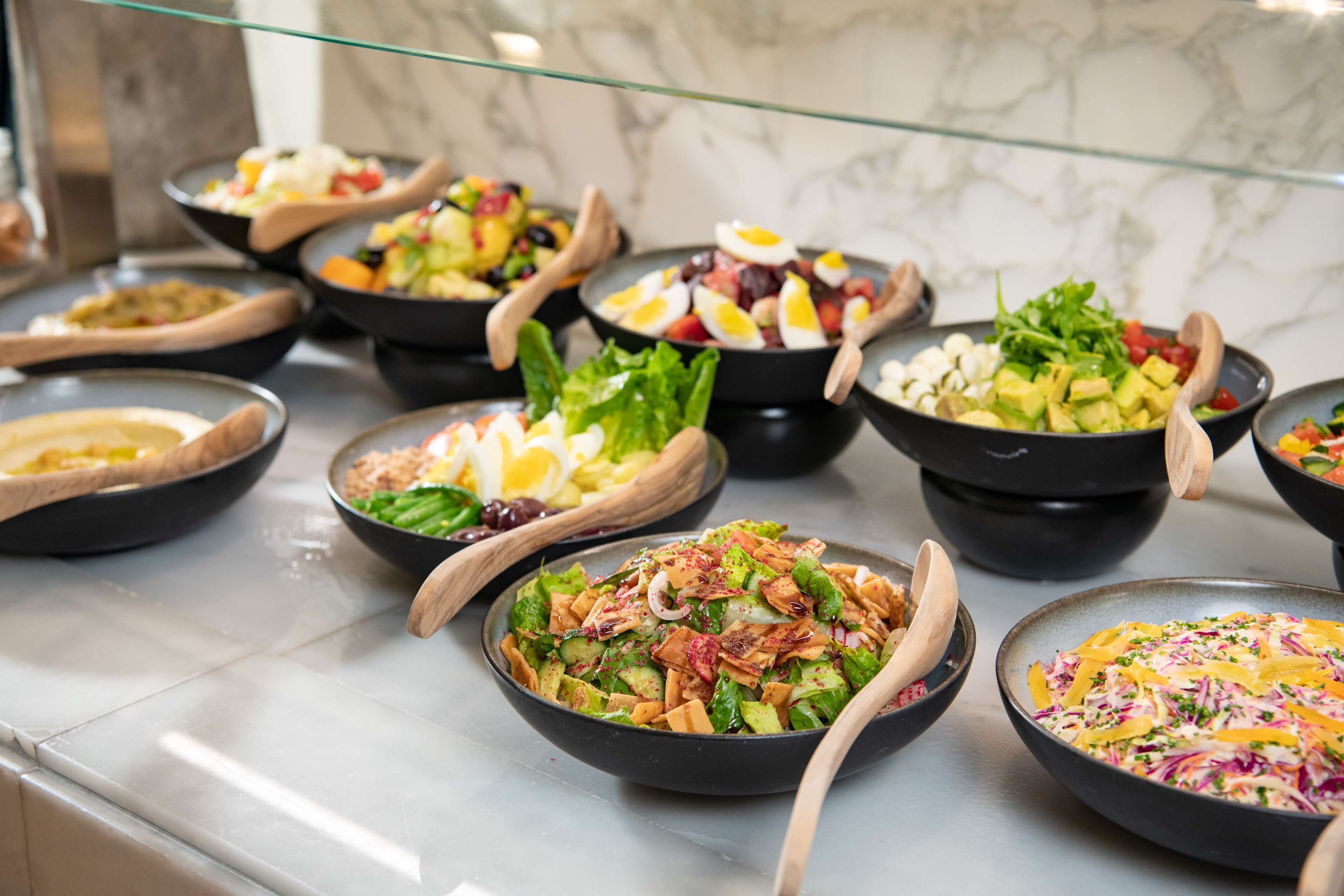 A buffet with various salads and dishes, including one with avocado and another with a mix of vegetables and nuts.