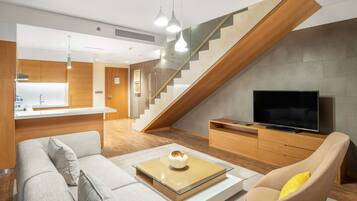Una sala de estar moderna con un sofá, una mesa de centro y un televisor. Una escalera conduce a un nivel superior.