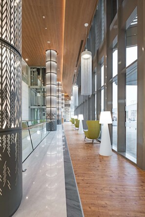 A modern interior with a wooden ceiling, large windows, and a row of green chairs with white lamps. - Radisson Blu Hotel & Residence, Riyadh Diplomatic Quarter (Riyadh)