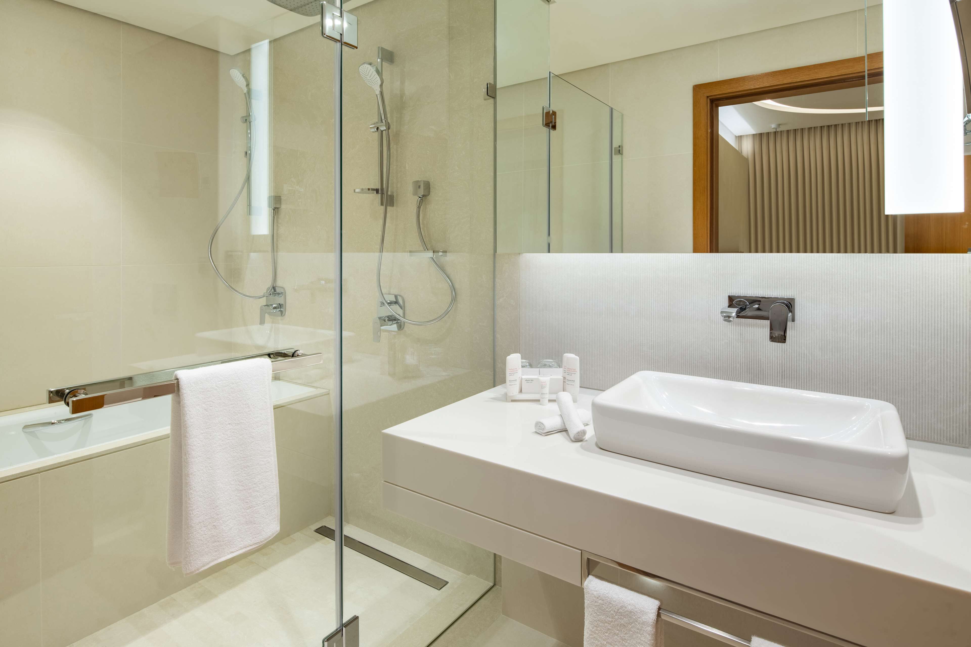 Un baño moderno con ducha de mampara de vidrio, un lavabo blanco y un espejo grande.