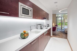 A modern kitchen with a microwave, sink, and a fruit bowl. There is a dining area with a chair and a table visible through a glass door.