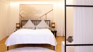 Ein Schlafzimmer mit einem großen Bett, zwei Nachttischen, einem Beistelltisch und einem dekorativen Zweig an der Wand.