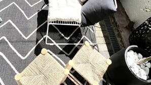 Eine Terrasse mit einem schwarz-weißen Zickzack-Teppich, zwei gepolsterten Stühlen mit Kissen, einem kleinen Tisch und Topfpflanzen.