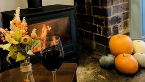 Una habitación acogedora con chimenea, un jarrón de vidrio con flores, una copa de vino y calabazas en el suelo.