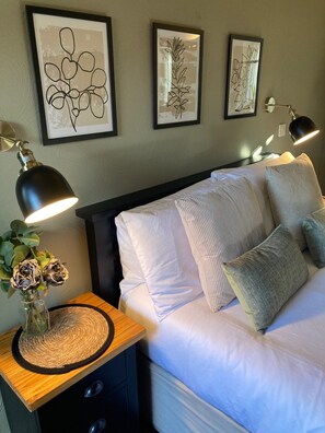 A neatly arranged bedroom with a bed, pillows, a bedside table with a lamp, and wall art.