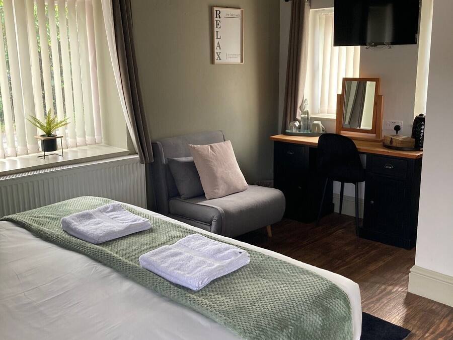 A bedroom with a bed, a desk, a chair, a television, and a window with curtains.