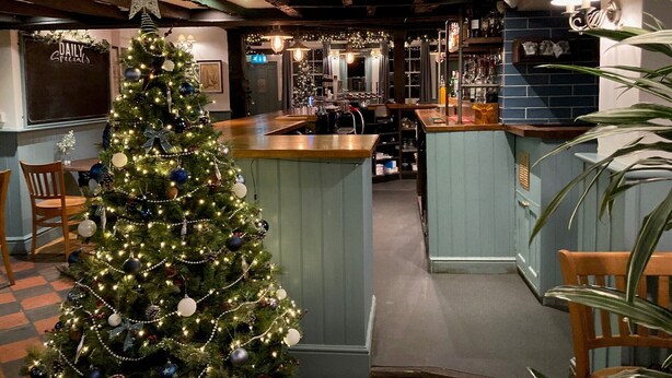 Un área de bar acogedora con un árbol de Navidad, mostrador de bar de madera y un techo rústico.