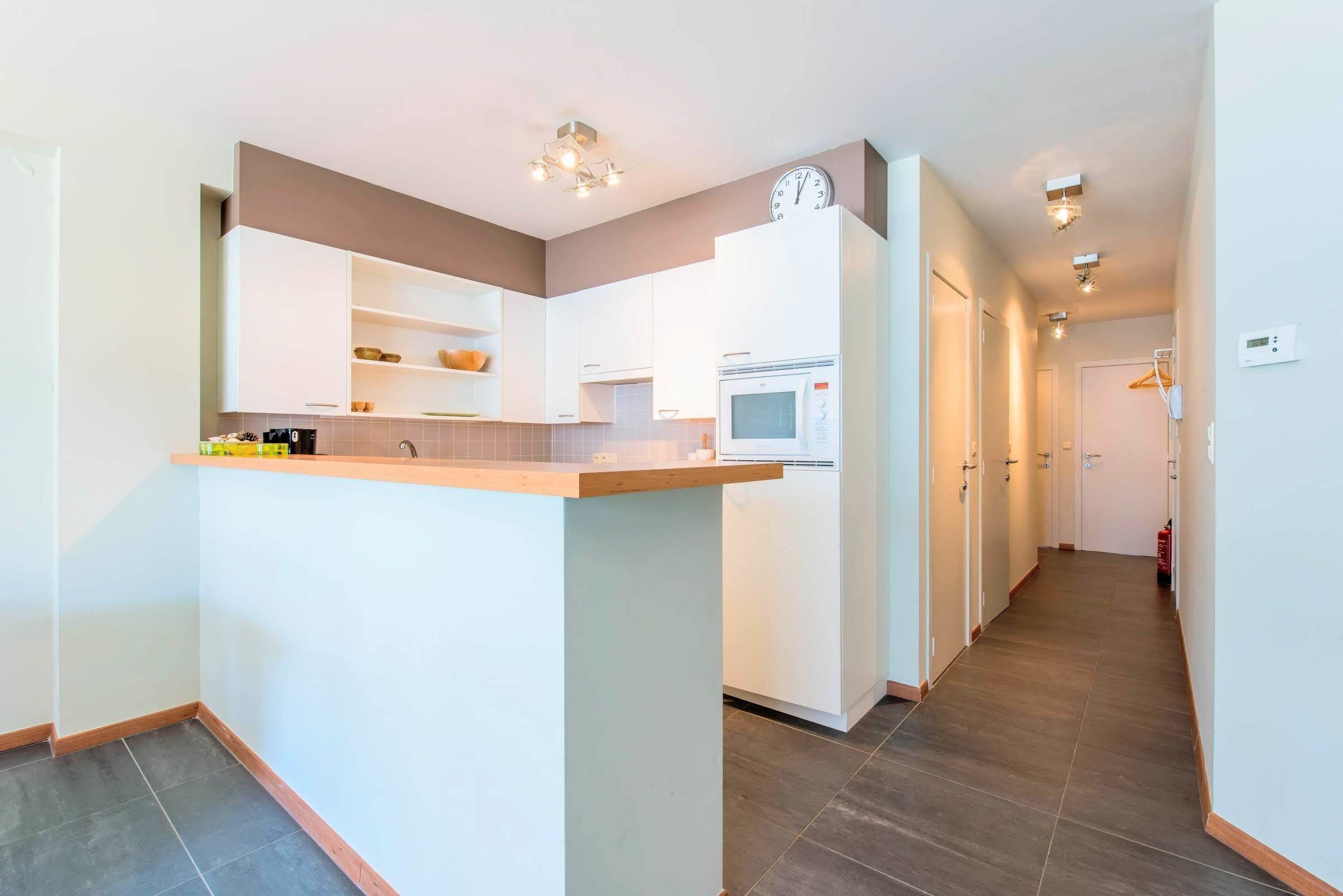 A modern kitchen with white cabinets, a wooden countertop, and a built-in microwave.