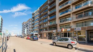 A multi-story building with balconies, a visible storefront, and parked cars on the street. - Ines 101 (Koksijde)