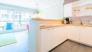A modern kitchen with white cabinets, a countertop, and a sink. There is a window providing natural light and a view of the outside. - Ines 101 (Koksijde)