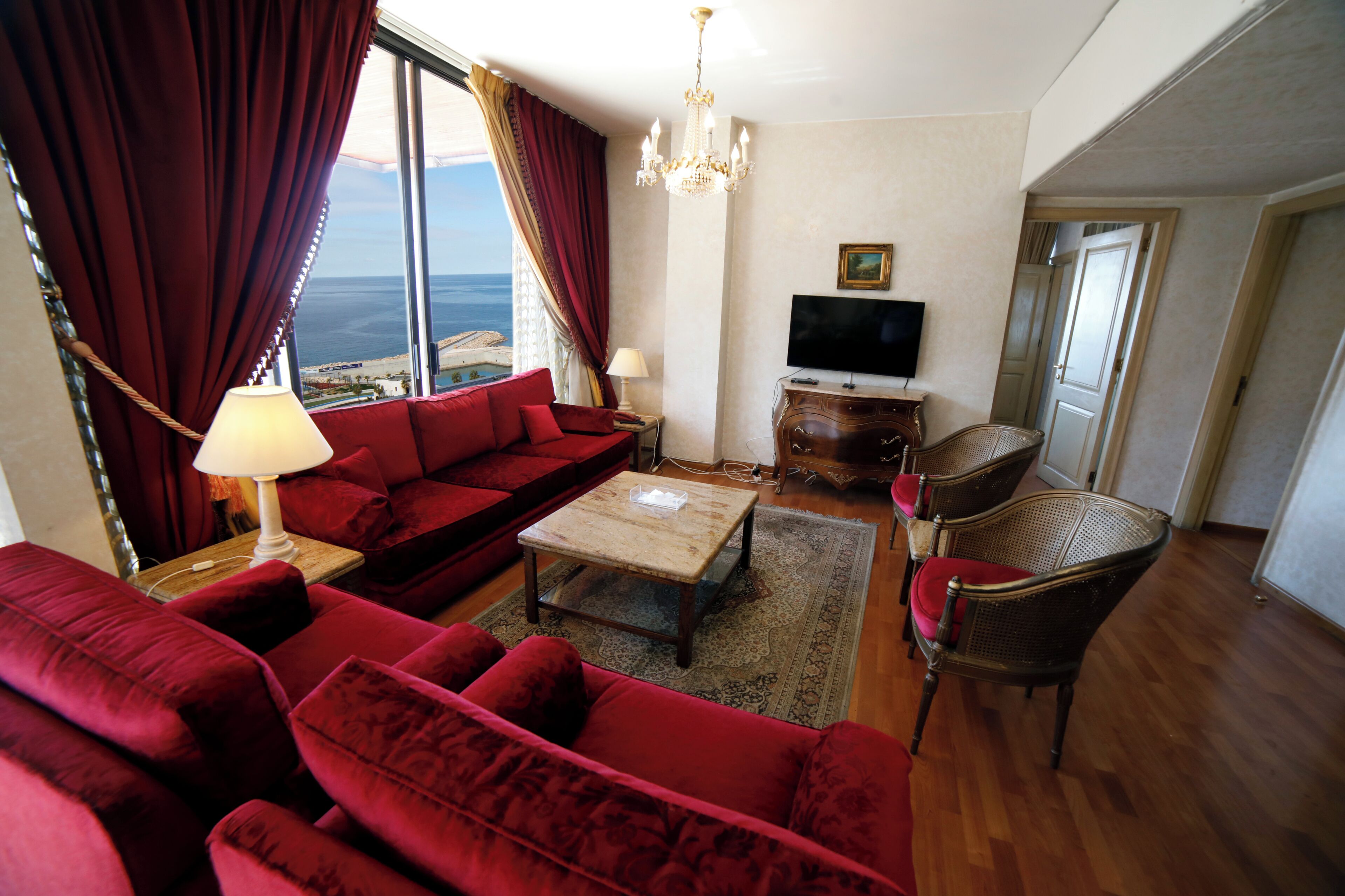 A living room with a red sofa, a wooden coffee table, a television, and wicker chairs.