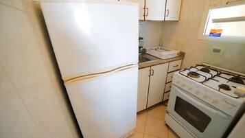 Una cocina con armarios blancos, un refrigerador blanco y una estufa con cuatro hornillas.
