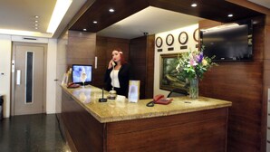 A reception desk with a flat-screen TV, a telephone, and a vase with flowers. - Holiday Home Suites (Beirut)