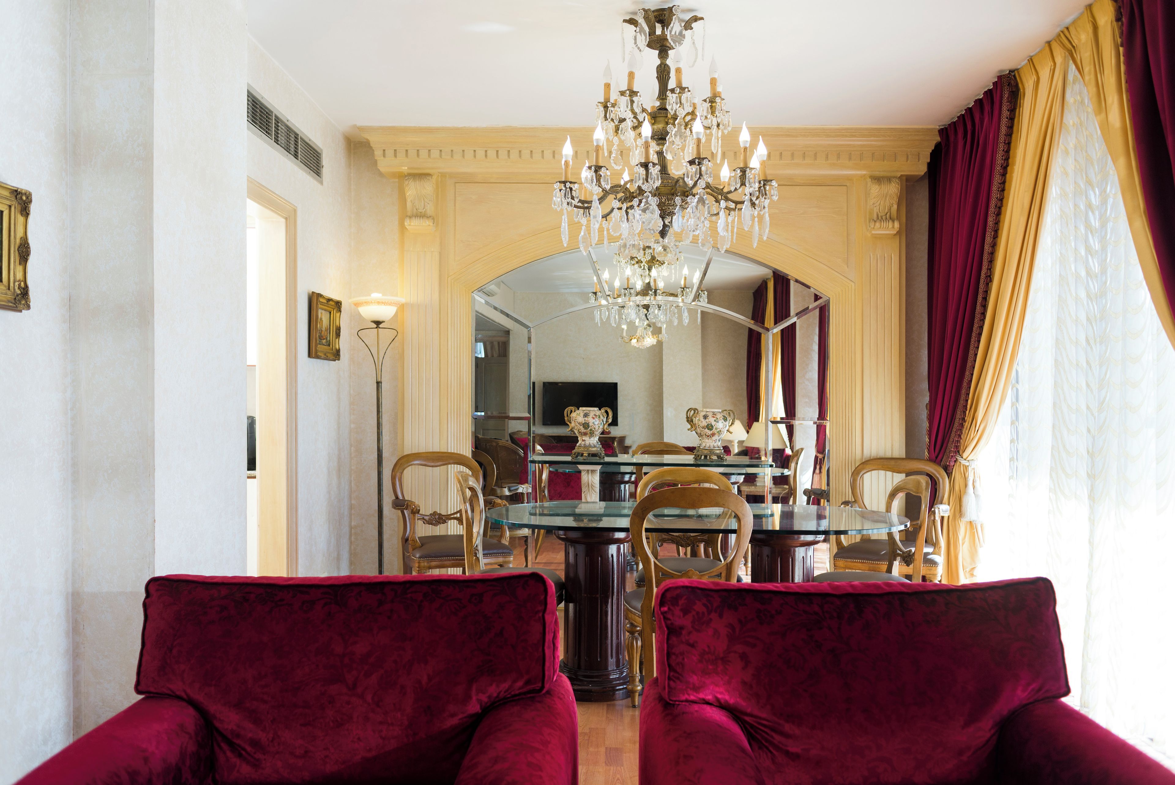 A dining area with a chandelier, red velvet chairs, and a glass-top table.