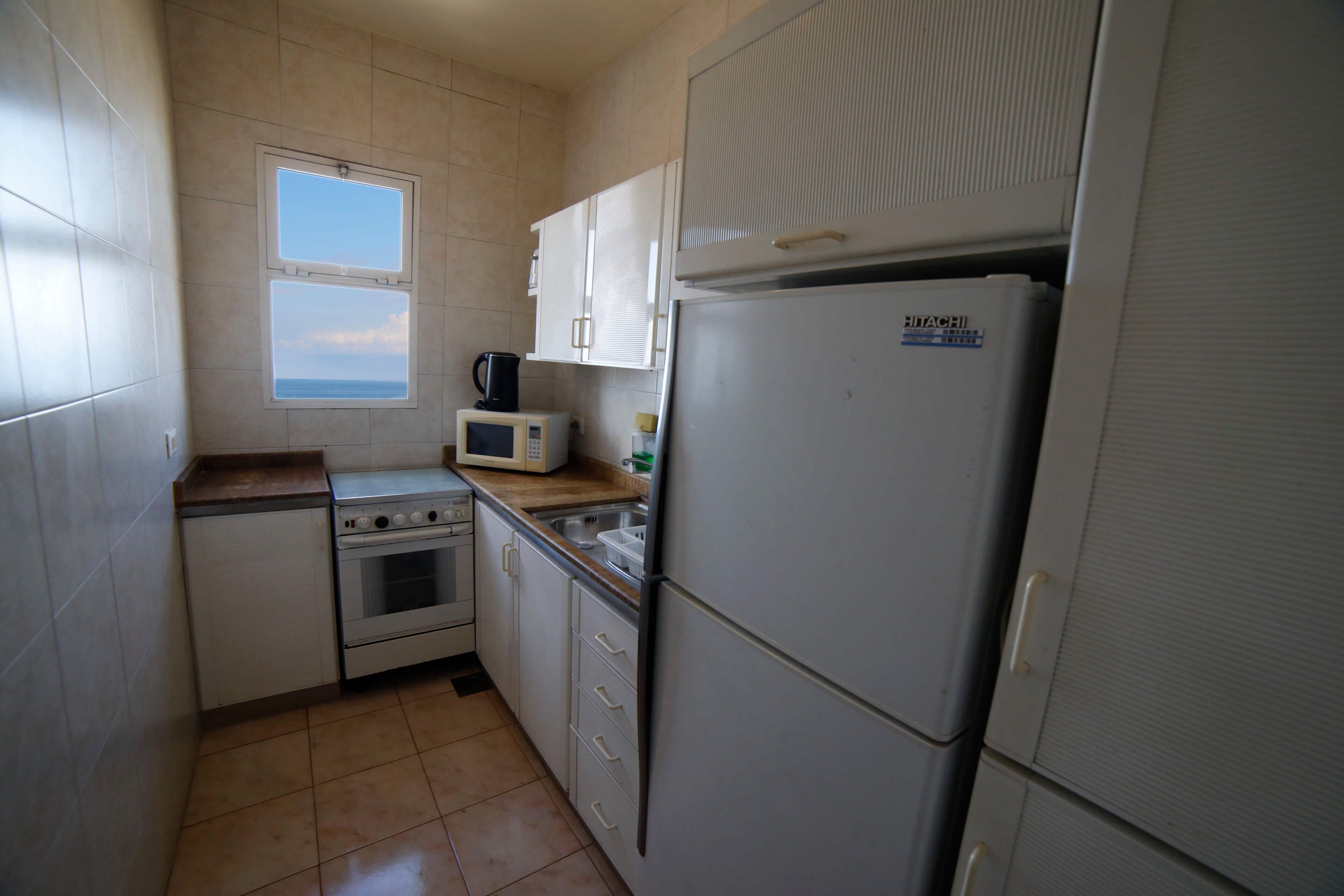 A compact kitchen with a stove, microwave, and refrigerator. There is a window providing a view of the sky.
