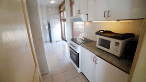 A kitchen with white cabinets, a stove, an oven, a microwave, and a window with blinds. - Holiday Home Suites (Beirut)