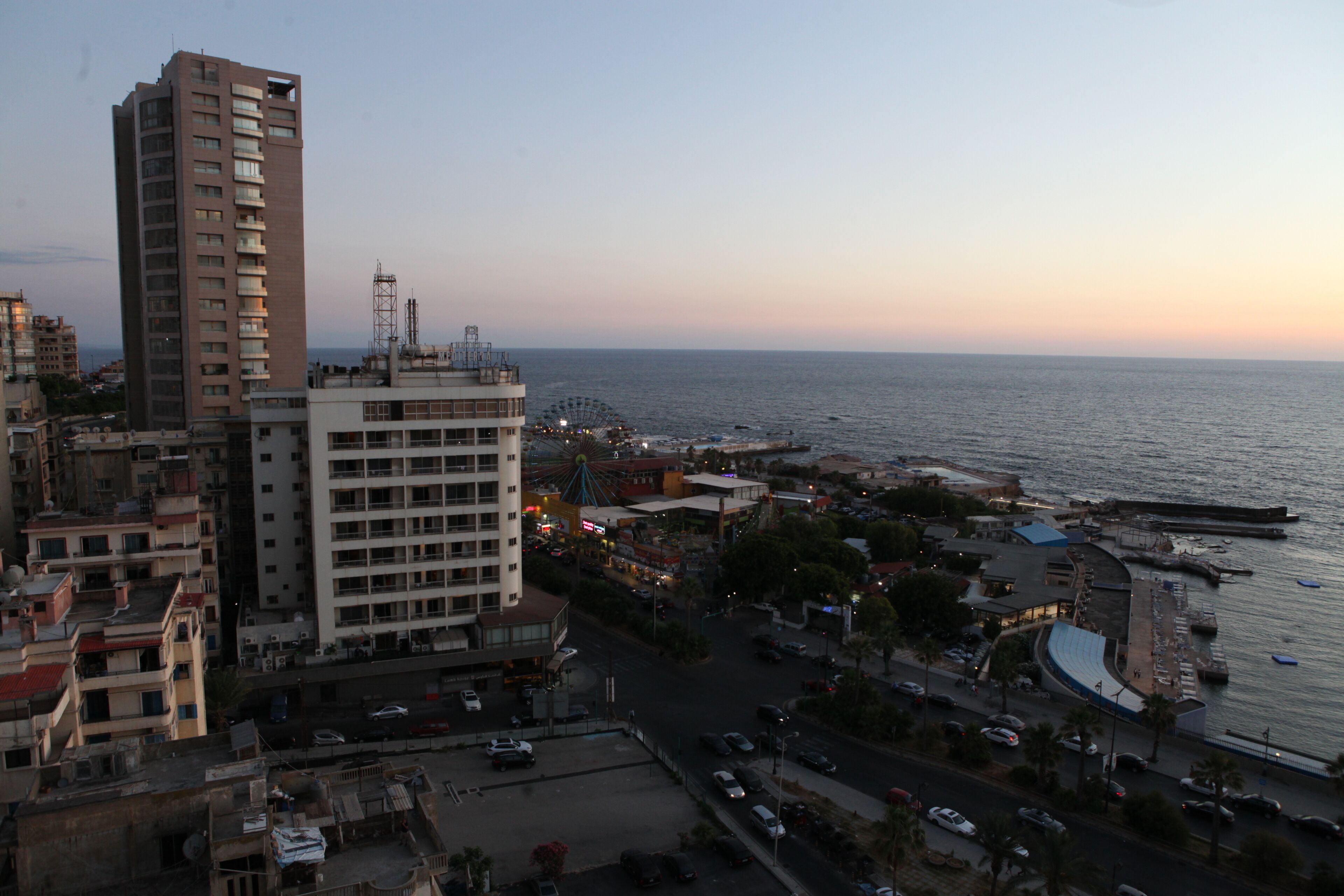 A coastal cityscape with high-rise buildings, a marina, and a waterfront promenade.