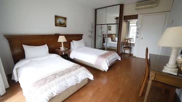 Ein Hotelzimmer mit zwei Betten, einem Holz-Kopfteil, einem Nachttisch mit Lampe, einem Spiegel und einem Esstisch mit Stühlen.