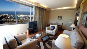A modern living room with a large TV, comfortable seating, and a view of the sea. - Holiday Home Suites (Beirut)
