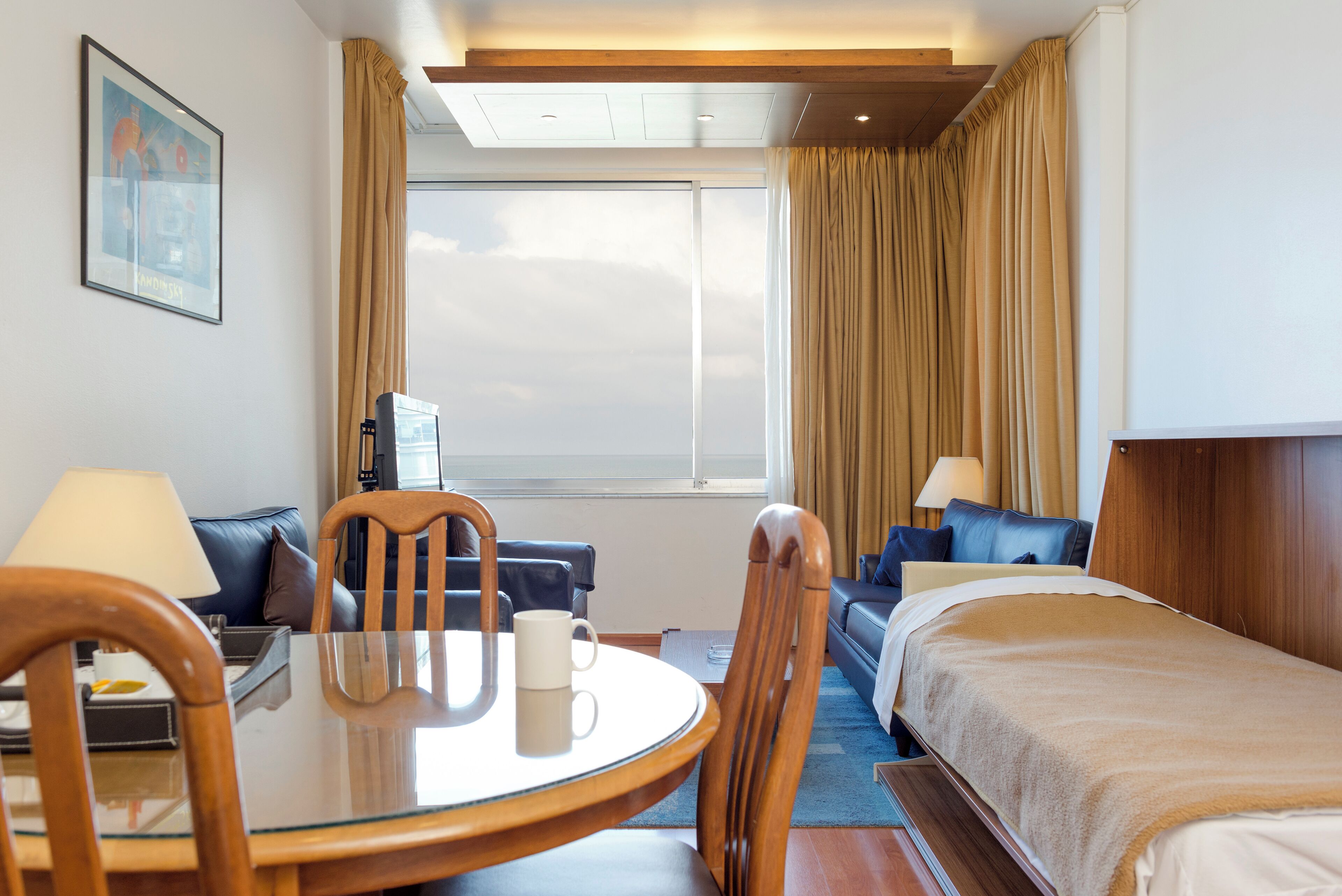 A hotel room with a bed, a desk with a chair, a dining table with a chair, and a window with curtains.
