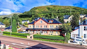 A guest house with a prominent sign, surrounded by lush greenery and a hill in the background.