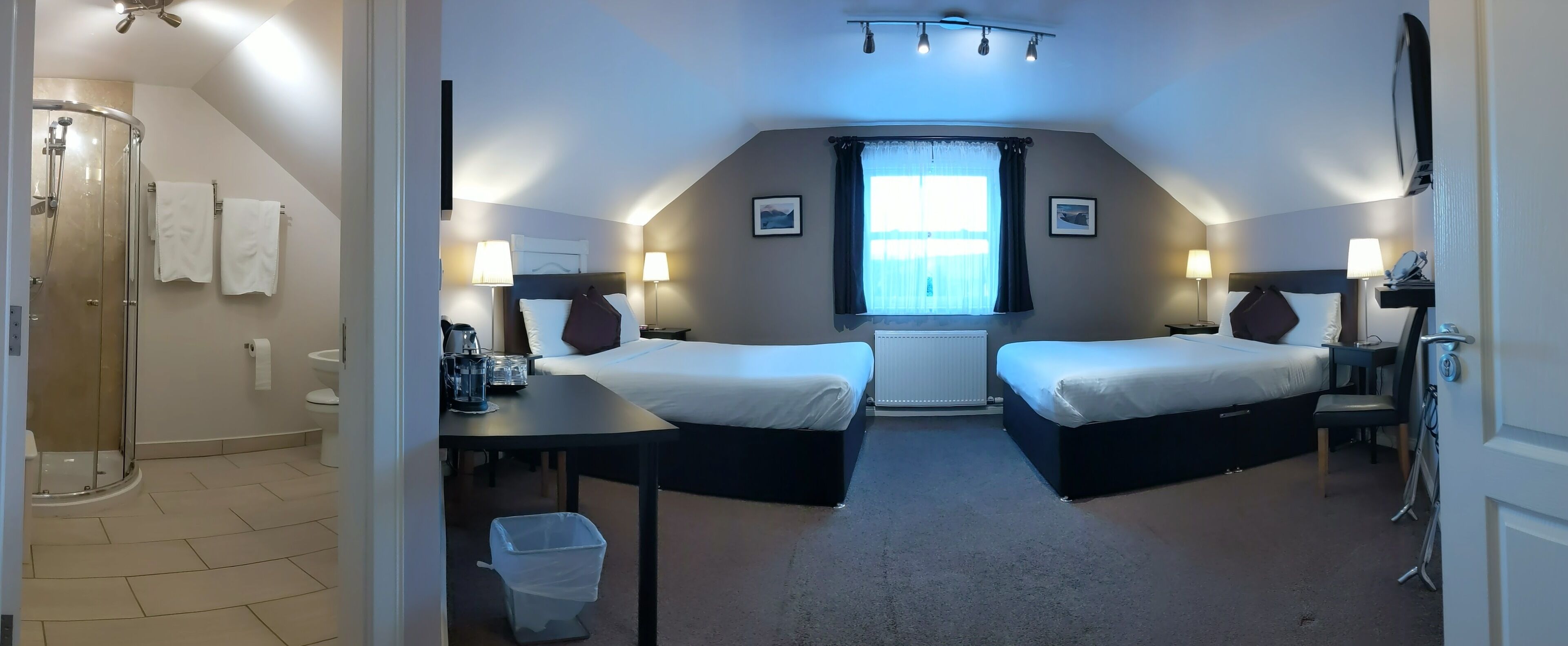 Une chambre d’hôtel avec deux lits, une douche, une petite table et une fenêtre avec des rideaux.