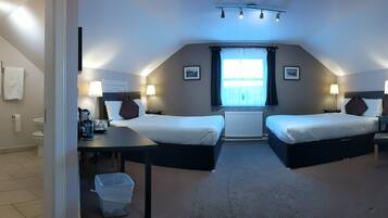 A hotel room with two beds, a shower, a small table, and a window with curtains.
