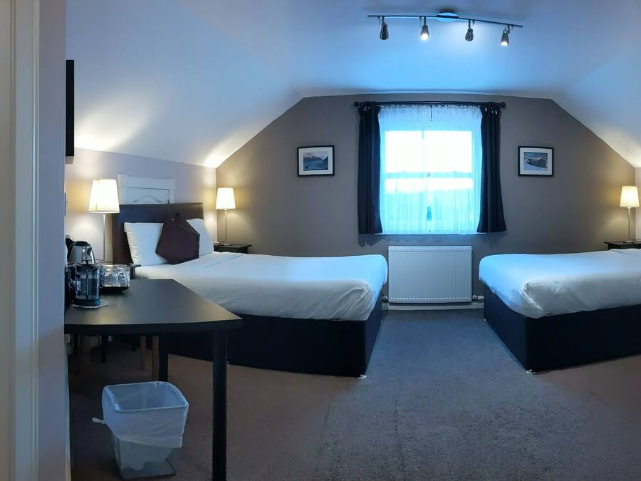 A hotel room with two beds, a shower, a small table, and a window with curtains.