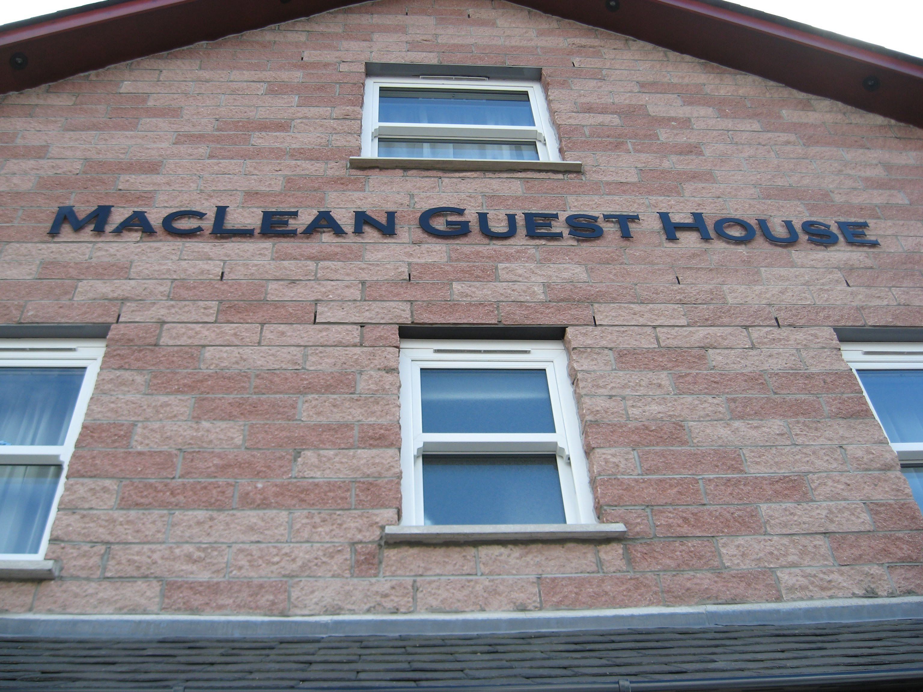 A brick building with the sign "MACLEAN GUEST HOUSE" above two windows.