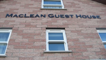 Un bâtiment en briques avec une enseigne indiquant « MACLEAN GUEST HOUSE » au-dessus de deux fenêtres.