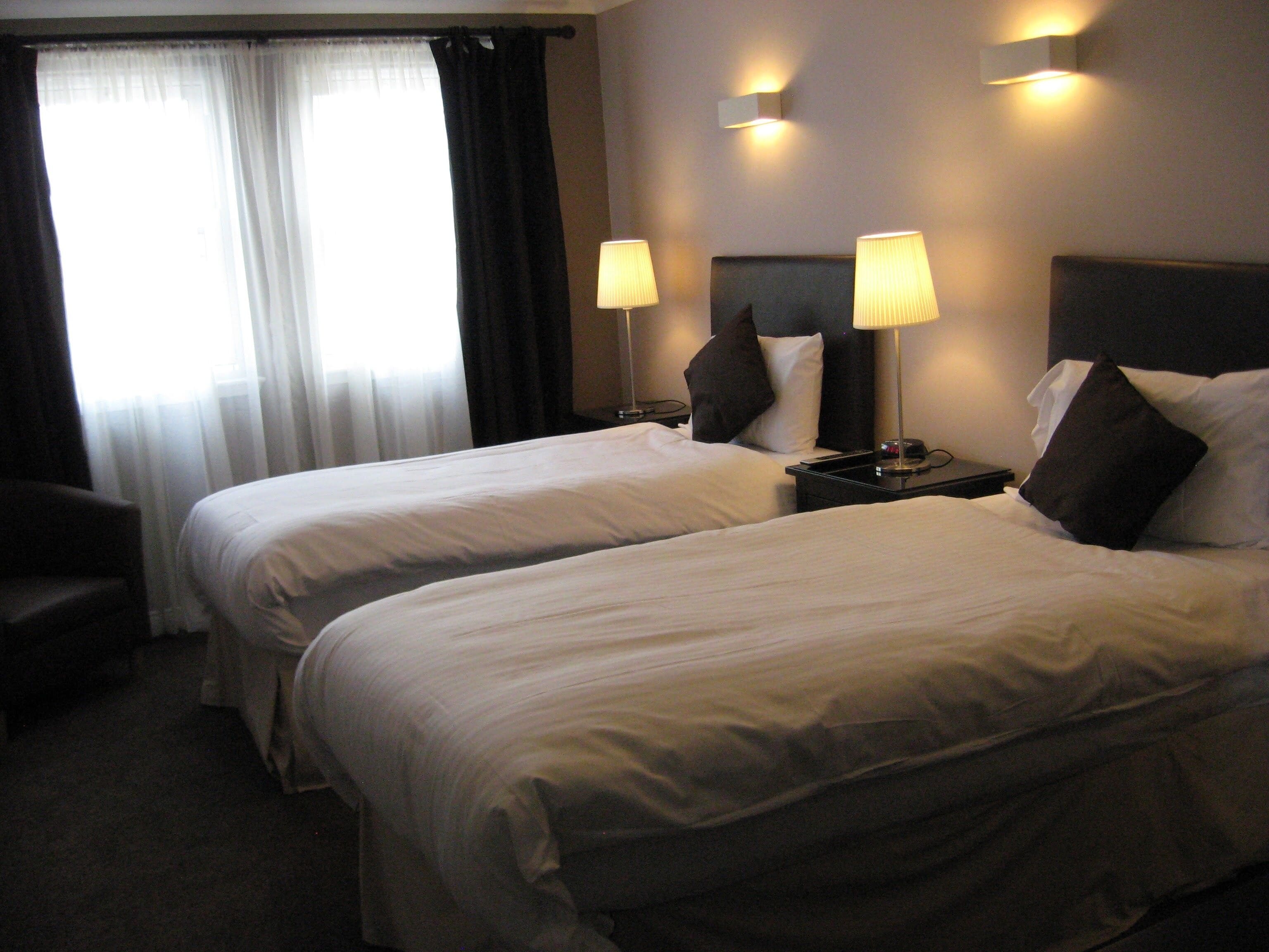 A hotel room with two beds, a chair, and two bedside lamps.