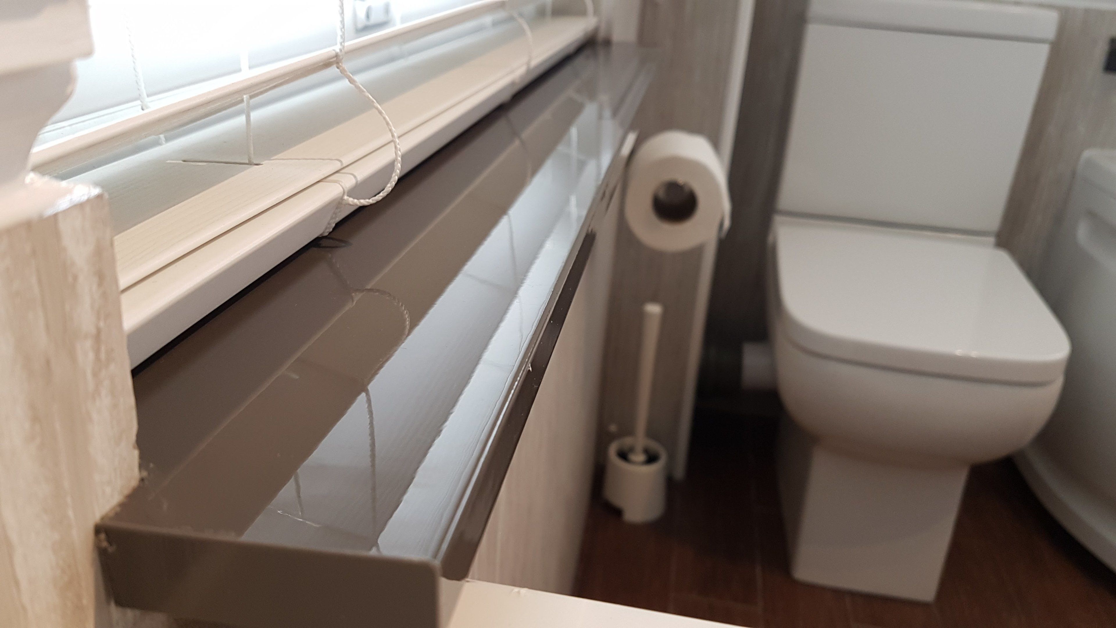 A bathroom with a toilet, a toilet paper holder, and a window with blinds.