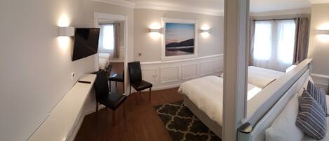Habitación de hotel con cama, escritorio, silla, televisión y ventana con cortinas.