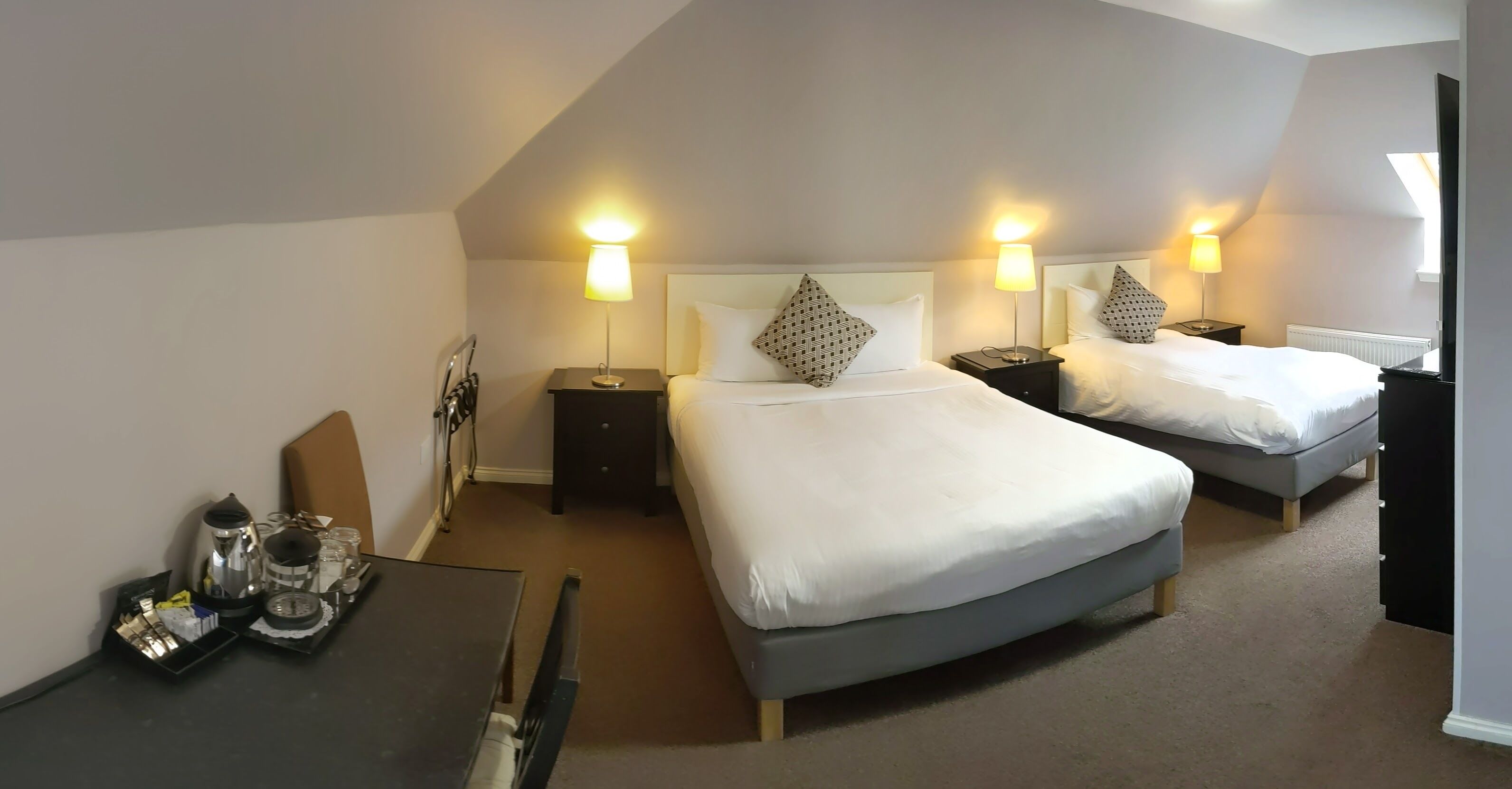 A hotel room with two beds, a desk with a coffee maker, and bedside lamps.