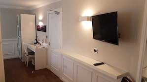 A hotel room with a white vanity, a mounted TV, and a small table with a remote control.