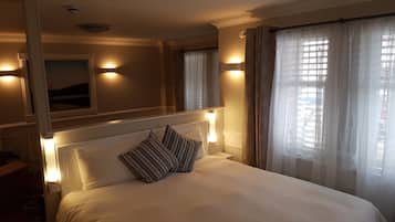 A hotel room with a large bed, two wall-mounted reading lamps, a window with sheer curtains, and a mirror above the bed.