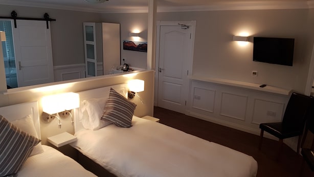 A hotel room with a bed, bedside tables, a mirror, a television, and a chair.